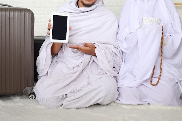 Corte de casal muçulmano sentado enquanto segura a tela do tablet, Al-Quran e tasbih. Pronto para Hajj ou