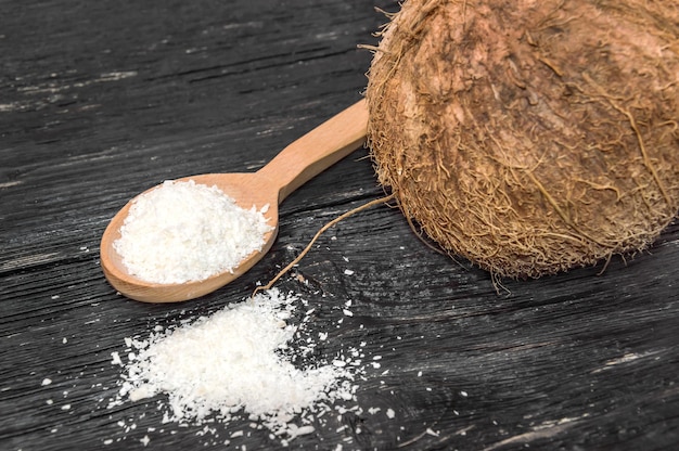 Corte de coco em uma colher de pau e coco na mesa de madeira preta.