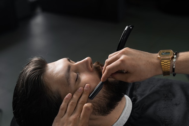 Corte de navalha do homem barba na barbearia. Homem barbeiro fazendo penteado para homem bonito.