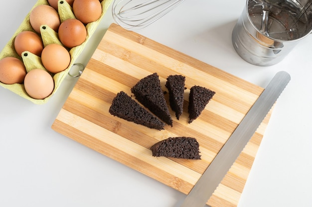 Corte de tábua de madeira com pedaços de bolo de chocolate Ovos de galinha em uma bandeja de reciclagem Batedor de massa