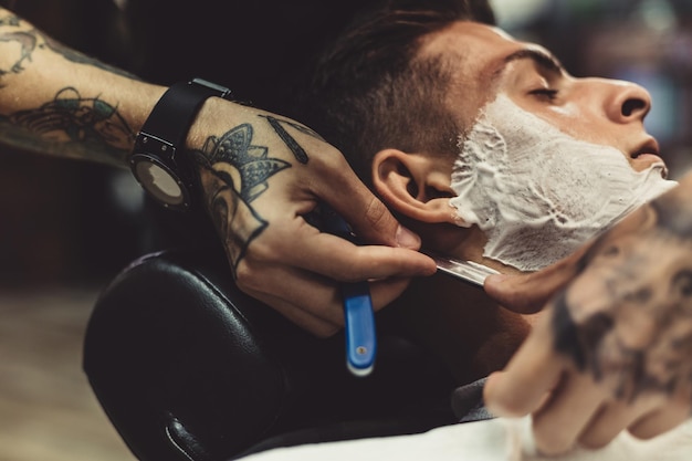 Corte elegante aplicação de espuma nas bochechas do cliente para barbear enquanto trabalha na barbearia