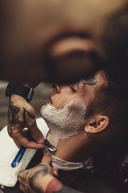 Corte elegante aplicação de espuma nas bochechas do cliente para barbear enquanto trabalha na barbearia