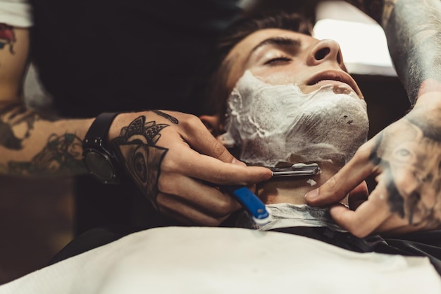 Corte elegante aplicação de espuma nas bochechas do cliente para barbear enquanto trabalha na barbearia