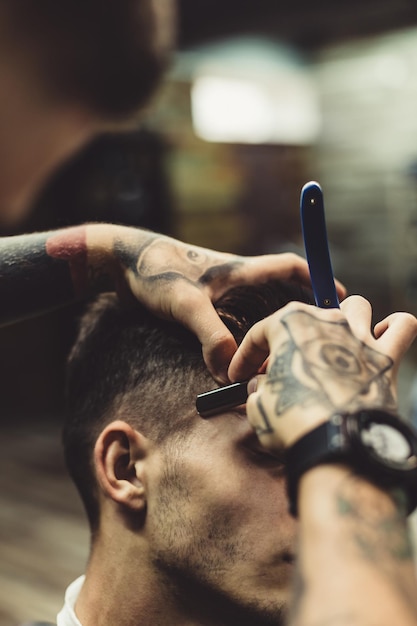 Corte elegante aplicação de espuma nas bochechas do cliente para barbear enquanto trabalha na barbearia