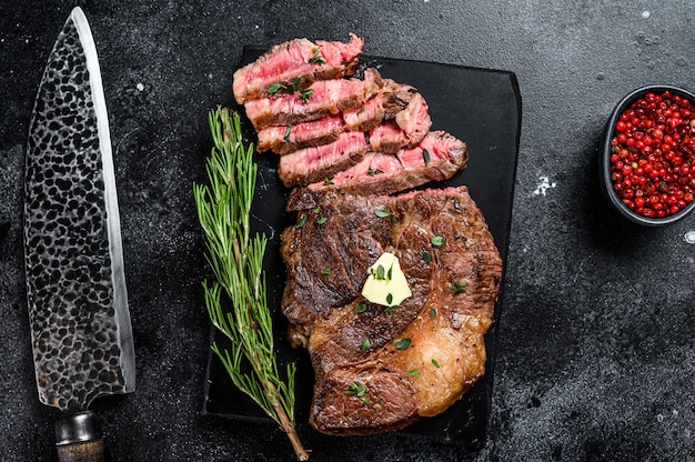 Corte el filete de carne de res a la parrilla en una tabla de mármol. Fondo negro. Vista superior.