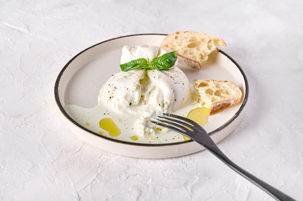 Corte italiano de queso burrata con pan ciabatta y aceite de oliva en la placa blanca con tenedor negro cerrar