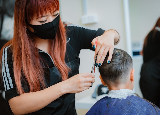 Corte o cabelo da criança para o cliente com medidas de segurança. estilista de cabelo asiático. Retomada do trabalho com medidas de segurança de barbearia no contexto da pandemia Covid-19