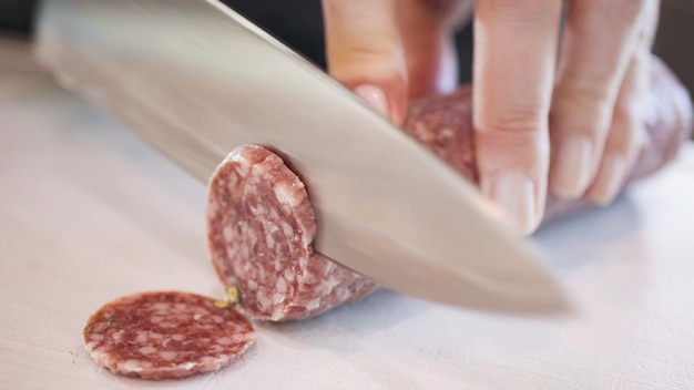 Corte o salame em anéis finos em uma tábua branca.