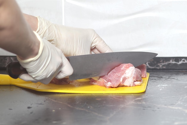 Corte pedaços de carne crua com uma faca grande em uma placa de corte fechada