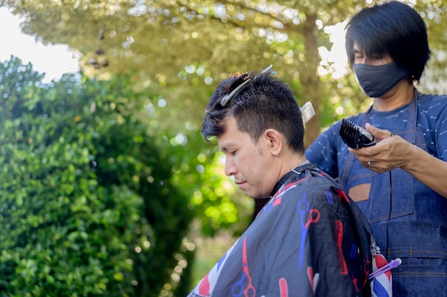 Corte de pelo asiático haciendo en el jardín de su casa. Aprender cursos de peluquería en línea durante el encierro para una nueva ocupación. Nueva vida normal después de la situación pandémica del brote de Covid-19.