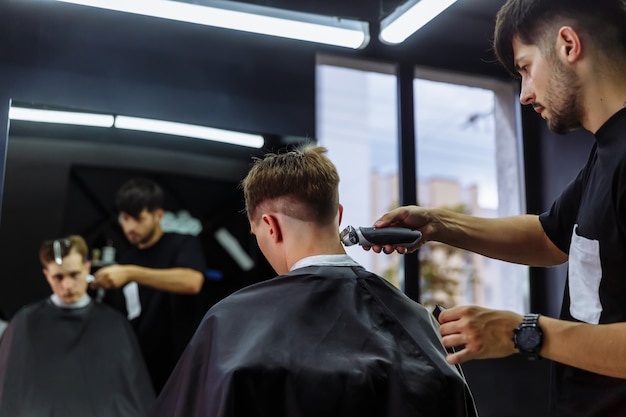 Foto corte de pelo masculino con maquinilla de afeitar eléctrica. barber hace el corte de pelo para el cliente en la peluquería usando un cortapelos. peluquería de hombre con máquina de afeitar eléctrica.