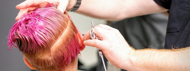 Corte de pelo de pelo húmedo teñido de rosa corto de una joven caucásica por un peluquero masculino en una barbería