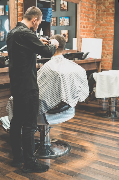 Corte de pelo en la peluquería. Barber corta el pelo en la cabeza del cliente. El proceso de creación de peinados para hombres. Un hombre en una barbería. El plan cercano. Estilista de equipos. Enfoque selectivo