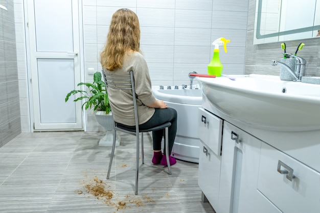 Corte de pelo de salón en casa durante la cuarentena. Chica con cabello largo está sentada en una silla en el baño, su cabello cortado en el piso a su alrededor. salones de belleza cerrados debido a la pandemia. Pasatiempo en casa, ocio.