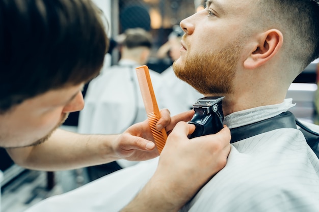 Foto corte de peluquero barbudo con máquina de afeitar