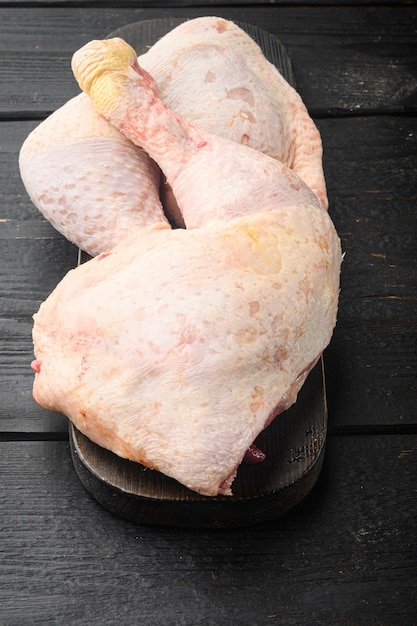 Corte primordial de coxas de frango cru, com conjunto de coxas e coxas de frango, na tábua de madeira, na mesa de madeira preta