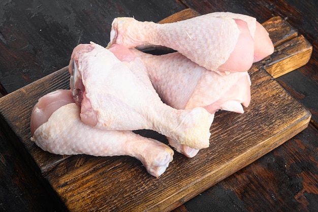 Corte primordial de coxas de frango cru, com conjunto de coxas e coxas de frango, na tábua de madeira, na velha mesa de madeira escura