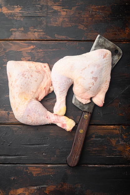 Corte primordial de coxas de frango cruas, com conjunto de coxas e coxas de frango, na velha faca de cutelo de açougueiro, na velha mesa de madeira escura