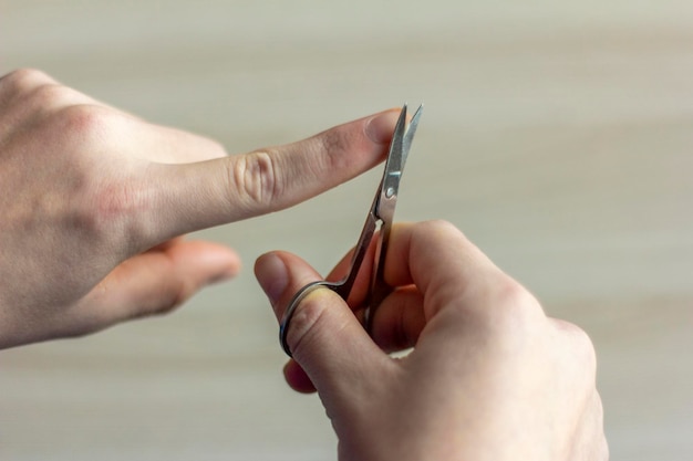 Corte suas unhas. Um jovem corta as unhas com uma tesoura de unha. Cuidando da sua aparência e de você mesmo.