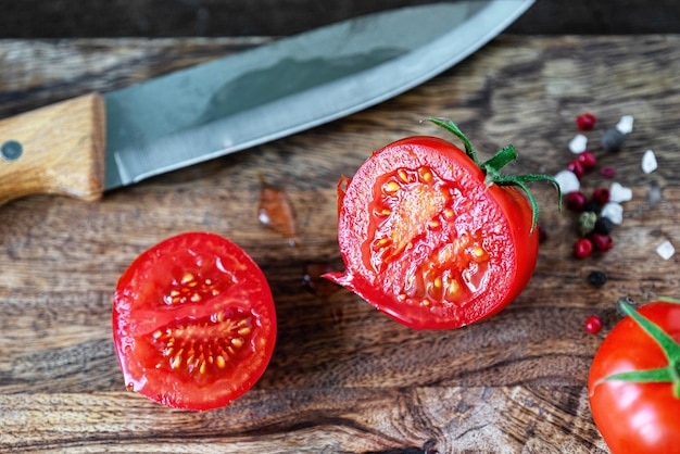 Foto corte el tomate rojo y el cuchillo de cocina sobre una tabla de cortar de madera oscura