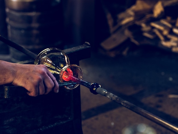 Corte um artesão masculino anônimo moldando o vidro em um vaso enquanto usa uma pinça de metal profissional e trabalha na oficina