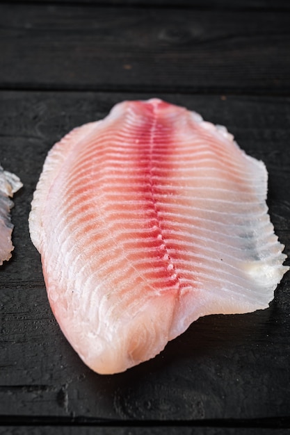 Cortes de carne de filete de pescado de tilapia, sobre mesa de madera negra