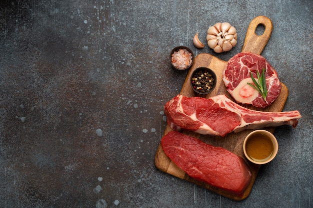 Cortes de carne surtidos y diferentes bistecs sobre tabla de madera, cuchillo de carnicero rústico desde arriba. Filete de ternera Tomahawk, pierna de ternera, filete. Corte de carne, restaurante steak house o concepto de carnicería, espacio de copia