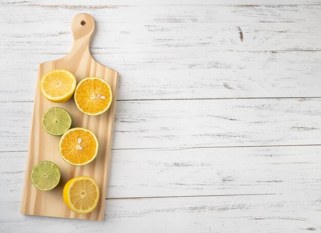 Cortes de laranja, limão verde e limão siciliano sobre uma placa de madeira com espaço de cópia.