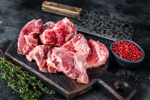 Cortes de estofado de carne de cordero cruda con hueso en tablero de carnicero de madera y cuchilla