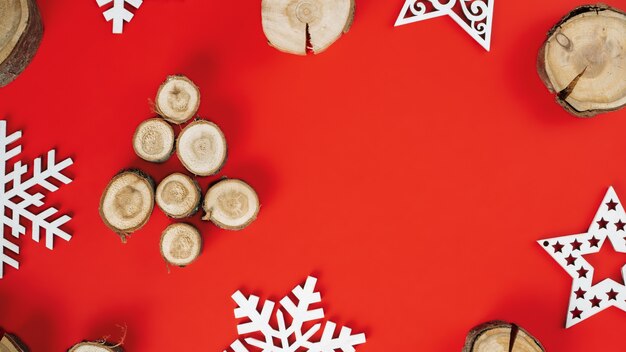 Cortes de madera o losas de ramas, dispuestas en forma de árbol de Navidad con copos de nieve de madera sobre fondo rojo. Bandera. Endecha plana. Copia espacio