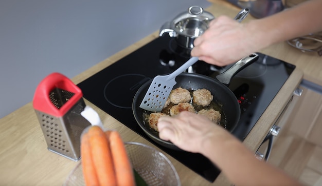 Cortilha frita nas mãos de um cozinheiro contra o fundo de uma frigideira e um fogão elétrico