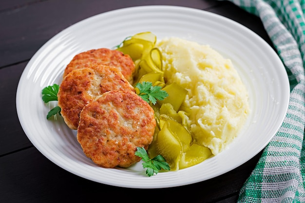 Cortillas de carne fritas caseras con puré de patatas y pepino encurtido en un plato blanco