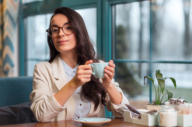 Cosa interesante. Bonita mujer pensativa concentrada sentada en el café mientras piensa y sostiene el café