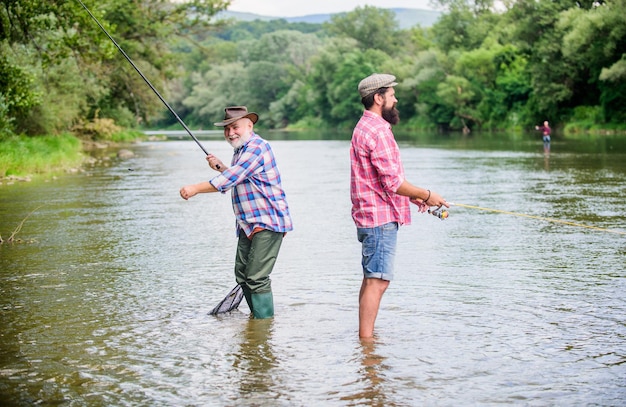 Cosas buenas para días buenos. fin de semana de verano. pescadores de hombres maduros. dos pescador feliz con caña de pescar y red. amistad masculina. Union familiar. padre e hijo pescando. actividad deportiva hobby. Cebo de trucha.