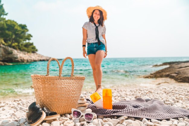 Cosas de playa sombrero de paja y bolsa con aletas y crema de protección solar en la orilla del mar mujer en el fondo
