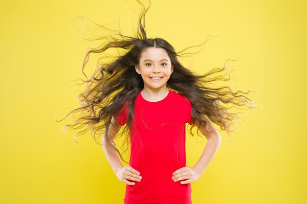 Cosas que haces para dañar tu cabello. Fondo amarillo del pelo largo ondulado del niño adorable de la muchacha. El viento también puede dañar el cabello. Los vientos fuertes y persistentes pueden crear enredos y enredos en el cabello largo ondulado y rizado.