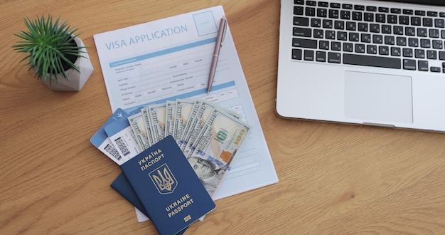 Cosas turísticas con dinero de pasaporte de solicitud de visa y boletos en escritorio de fondo de madera con computadora portátil Vista superior