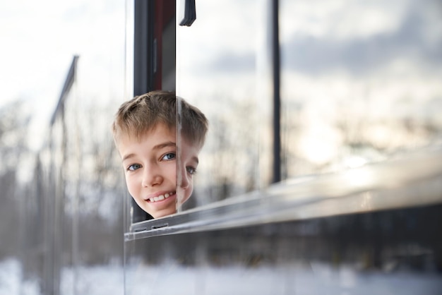 Foto cosecha de divertido niño varón sonriendo mirando a la cámara inclinando la cabeza hacia fuera vista frontal del autobús moderno gris