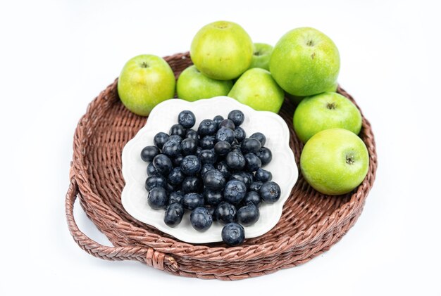 Cosecha de verano de arándanos maduros frescos y manzanas verdes en una canasta sobre fondo blanco.