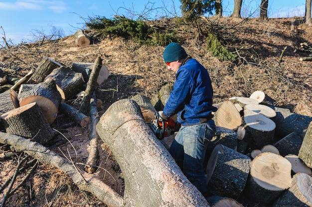 Cosechando leña para el invierno, un hombre con anteojos cortó un árbol con una motosierra sosteniéndolo en sus manos