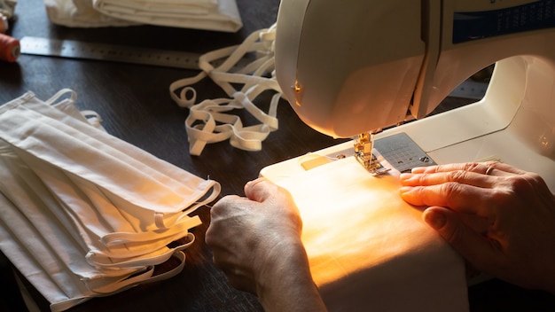 Coser máscaras protectoras antivirus en casa. Mujer cose máscaras en una máquina de coser