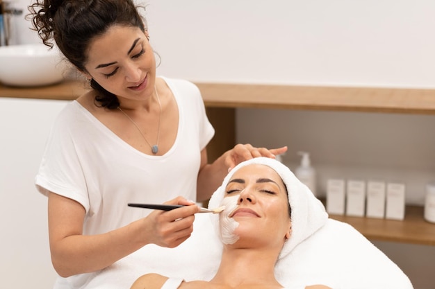 Cosmética aplicando creme no rosto da mulher no spa