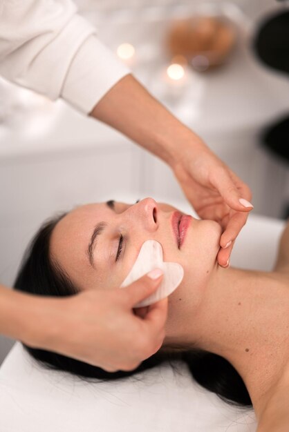 Cosmética de colheita fazendo massagem facial com gua sha para cliente feminina