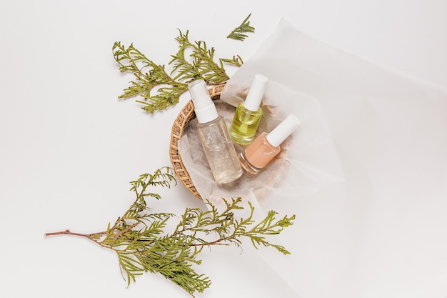 Cosmética ecológica con planta. Endecha plana, botella de bomba de vidrio transparente de vista superior, frasco de cepillo, frasco de suero hidratante en una canasta de papel sobre un fondo blanco. SPA cosmética natural