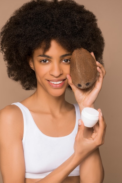 Cosmética natural. Mulata de pelo rizado sosteniendo un coco y un tarro de crema