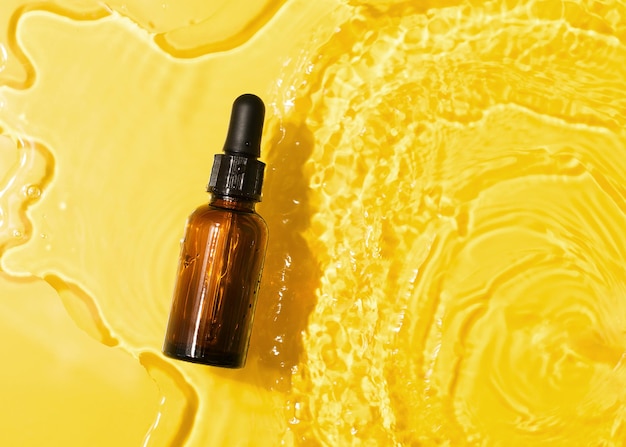 Cosmético de óleo de soro de garrafa em água limpa e transparente com luz solar em fundo amarelo