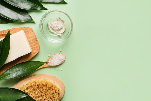 Cosmético orgânico natural e escova de banho plana com folhas em fundo verde menta