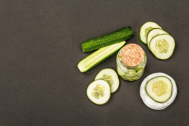 Cosméticos caseros de pepino. Mascarillas desintoxicantes de piel vegetal. Loción facial natural o agua tónica. Fondo negro mate, vista superior