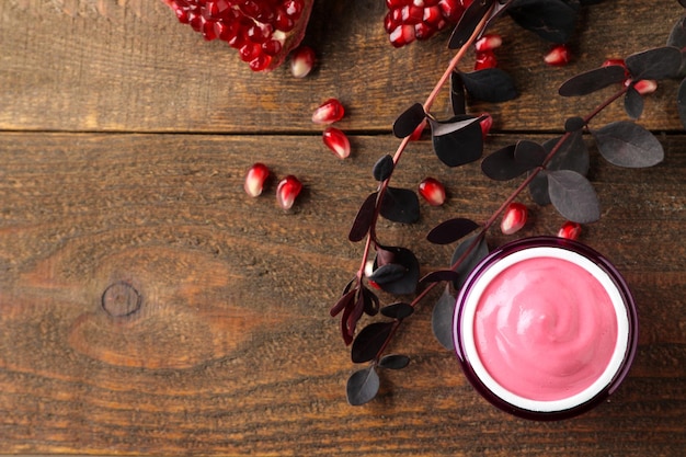 Cosméticos en crema para la cara y el cuerpo Crema rosa y ramas floridas y granada en un frasco morado sobre una mesa de madera marrón vista superior