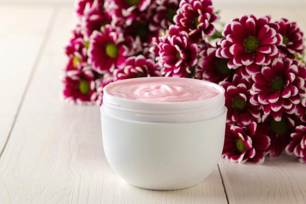 Cosméticos creme para rosto e corpo Creme rosa e flor em uma jarra branca em uma mesa de madeira branca